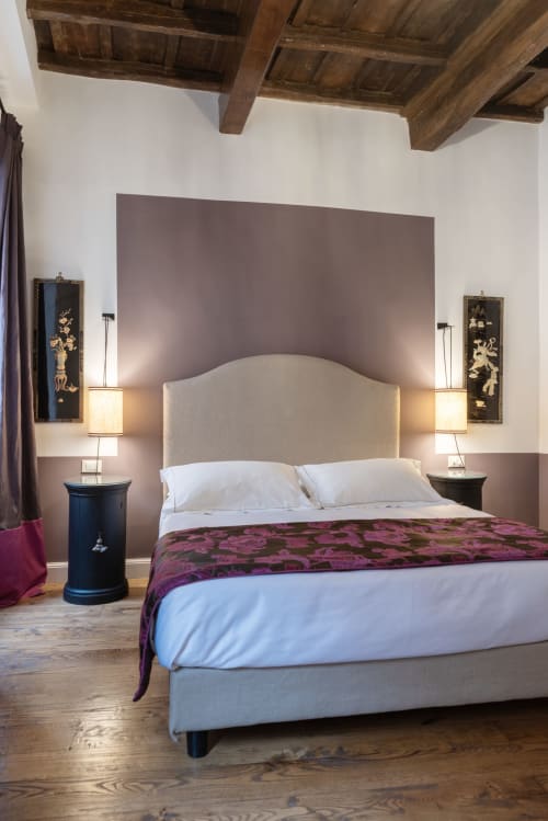 Camera elegante alle Residenze Clodio Roma con testata color crema, biancheria viola, travi in legno e arte asiatica alle pareti