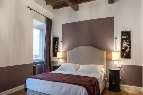Camera moderna a Residenze Clodio vicino la Scalinata di Spagna a Roma con testata beige, plaid bordeaux, travi in legno e vista città