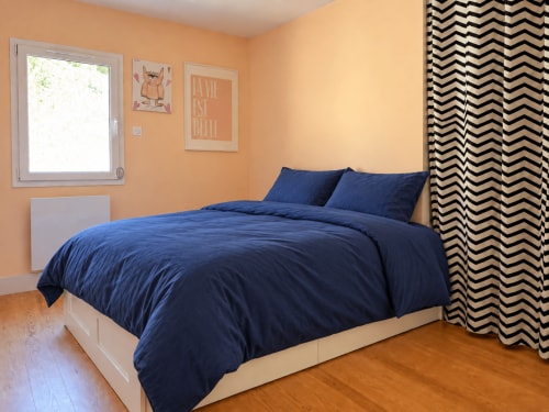 Chambre lumineuse avec literie bleu marine, murs pêche, rideaux à chevrons et vue sur le jardin à la villa Marcel Vacances