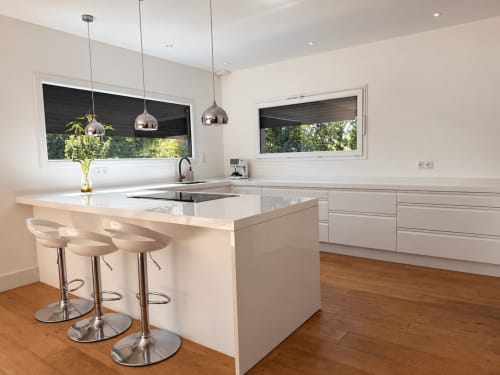 Cuisine moderne avec meubles blancs, îlot de repas, luminaires suspendus et vue sur jardin à la villa Marcel Vacances