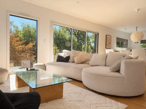 Salon de villa moderne avec canapé beige courbe, vue sur jardin et lumière naturelle à Marcel Vacances, Banassac-Canilhac