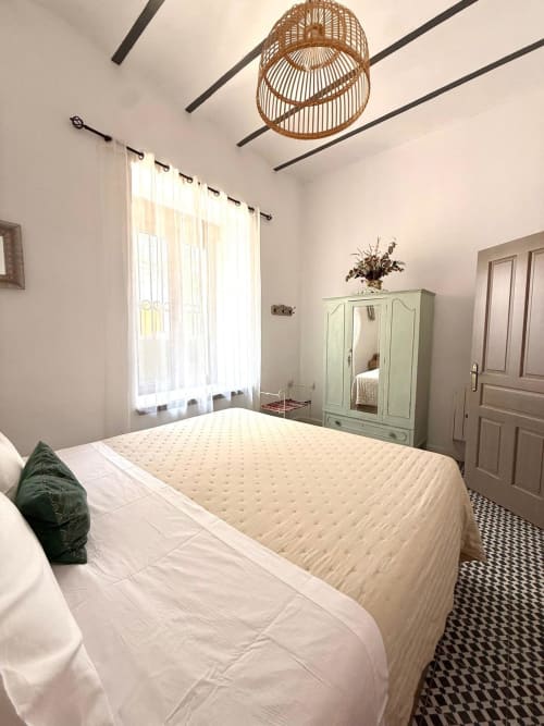 Dormitorio luminoso del apartamento deluxe de Casa Turística San Agustín en Córdoba, con ropa de cama crema, armario menta y lámpara tejida