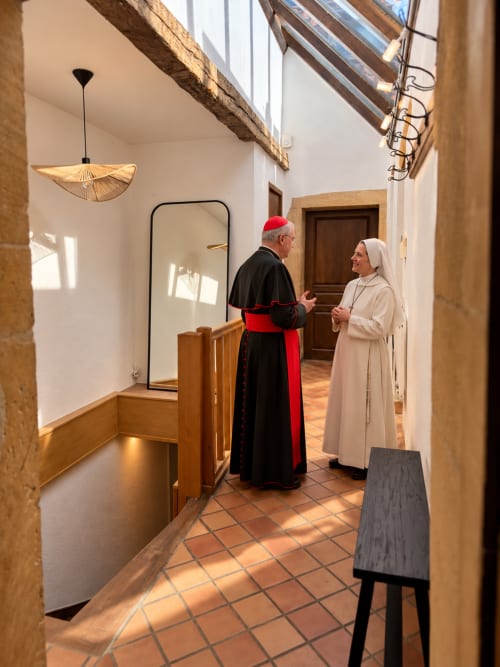 Two religious figures in traditional attire conversing in bright hallway of La suite papale apartment hotel in Metz, France