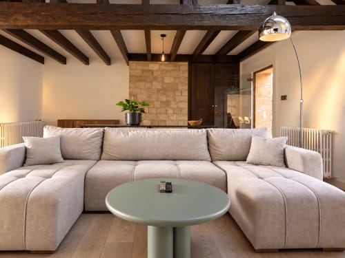 Modern beige sectional sofa in Metz apartment living room with exposed wooden beams and sage green side table