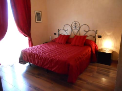 Camera elegante dell'Hotel Villa Moderna a Genova con biancheria rossa, testata ornamentale in metallo e illuminazione calda