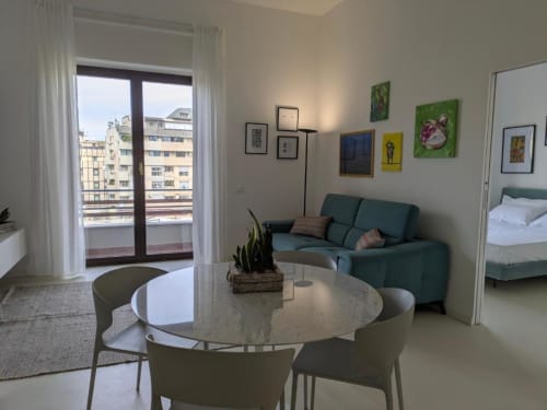Soggiorno moderno a Palermo con tavolo rotondo, divano verde, vista sulla città dal balcone e opere d'arte colorate