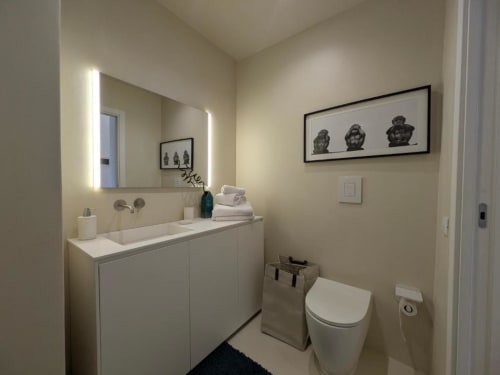 Bagno moderno nell'appartamento di Palermo con vanity bianca, specchio illuminato, wc e quadri su pareti color crema