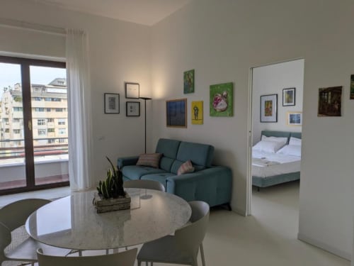 Soggiorno moderno con divano teal, tavolo da pranzo e balcone con vista sulla città nella suite dell'hotel BnB del Parlamento a Palermo