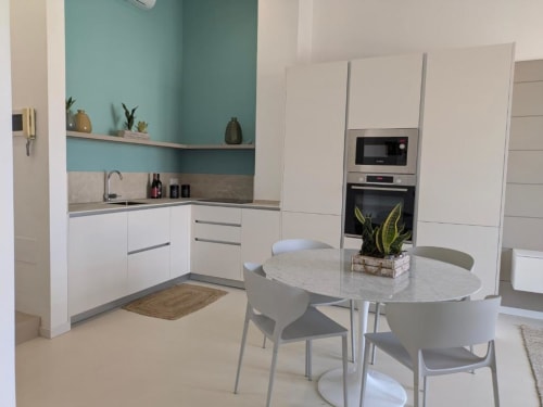 Cucina e zona pranzo moderna nell'appartamento di Palermo con mobili bianchi, parete azzurra e tavolo rotondo