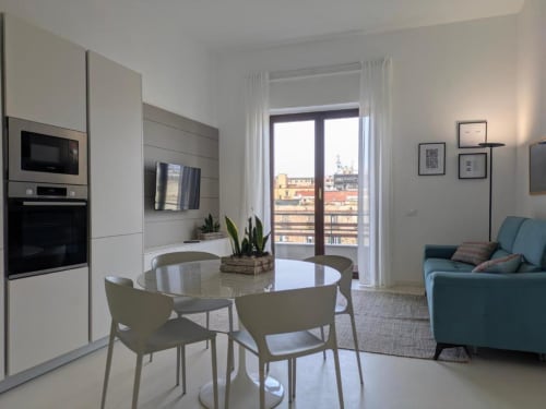 Moderno appartamento a Palermo con cucina a vista, tavolo da pranzo, divano azzurro e balcone con vista sulla città