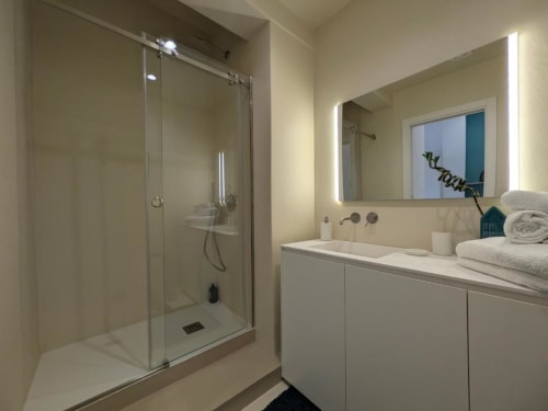 Moderno bagno nell'appartamento di Palermo con box doccia in vetro, mobile bianco, specchio illuminato e asciugamani
