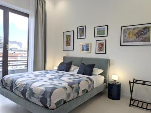 Camera moderna di BnB del Parlamento Palermo con letto imbottito grigio, biancheria geometrica, opere d'arte incorniciate e balcone con vista città