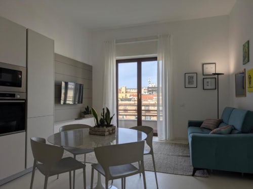 Cucina moderna e zona living con vista sulla città di Palermo dal balcone, tavolo da pranzo, divano e acciaio inox