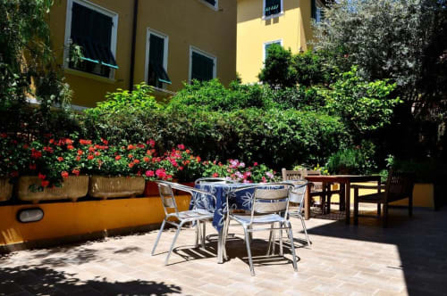 Soleggiato patio della corte dell'Hotel Villa Moderna a Genova con tavolo da pranzo, fiori colorati e edificio giallo
