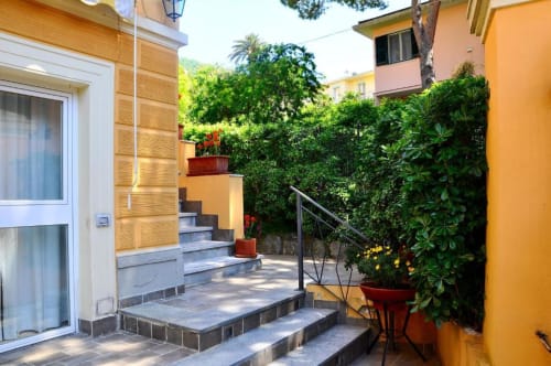 Terrazza soleggiata dell'Hotel Villa Moderna a Genova con muri gialli, piante in vaso e gradini in pietra verso l'alto