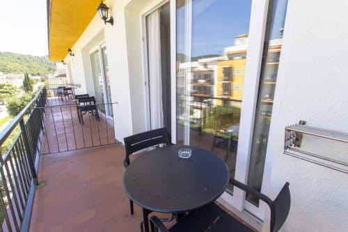 Amplio balcón del hotel El Sol II en Tossa de Mar con mesa redonda, sillas y vistas a la ladera