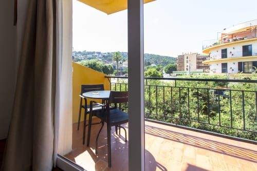 Balcón soleado con toldo amarillo, sillas negras y vistas a la montaña en el hotel El Sol II de Tossa de Mar