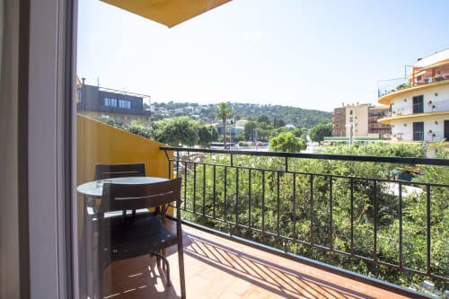 Balcón soleado del hotel El Sol II en Tossa de Mar con mesa de comedor, vistas a las montañas y exuberante vegetación