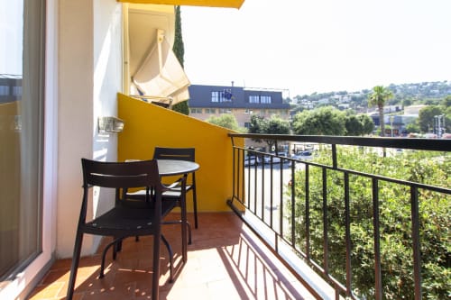 Balcón soleado con toldo amarillo, sillas negras y vista a la ciudad del hotel El Sol II en Tossa de Mar, Girona