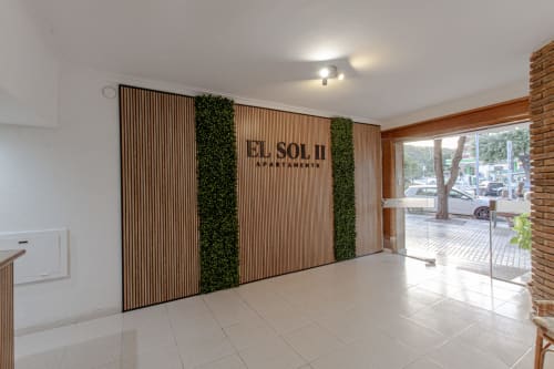 Entrada moderna del hotel El Sol II en Tossa de Mar con pared de lamas de madera, plantas verdes y suelo de azulejos brillante