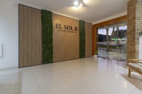 Entrada moderna del vestíbulo de apartamentos El Sol II en Tossa de Mar con pared de lamas de madera y plantas verdes