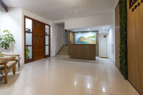 Moderno vestíbulo del hotel El Sol II en Tossa de Mar con suelo de azulejos, puerta de madera, arte costero y acentos verdes en las paredes