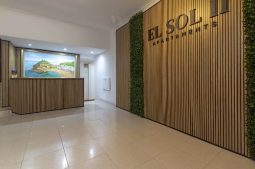 Recepción del hotel El Sol II en Tossa de Mar con paneles de madera modernos, pisos pulidos y vista de paisaje costero