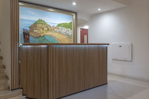 Loft hotelero moderno con mostrador de recepción curvo en madera, exposición iluminada de arte de la villa costera de Tossa de Mar, y diseño minimalista