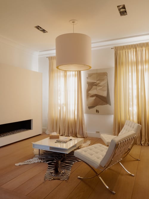 Modern sitting area in Bernard Suite at Castanea Business & Suites with pendant lamp, white chairs, fireplace, and golden
