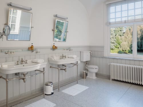 Luxury bathroom in Bernard Suite at Castanea Business & Suites with dual sinks, garden views, and classic vintage fixtures in