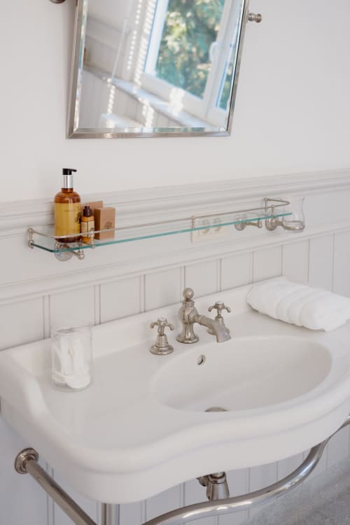 Elegant bathroom in Bernard Suite at Castanea Business & Suites with white pedestal sink, vintage faucet, and glass shelf