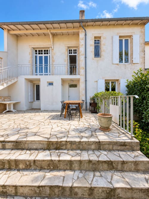 Cour de la Villa Cognehors à La Rochelle : patio en pierre, table de repas en bois, volets blancs et verdure luxuriante