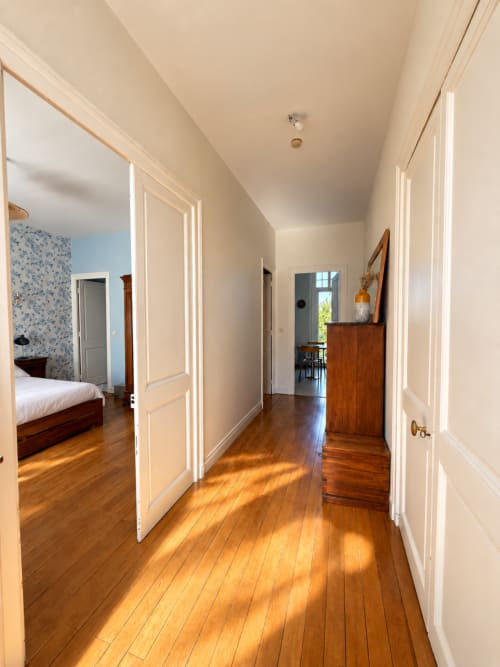Couloir lumineux de la villa ARLOÉ à La Rochelle avec parquet, murs crème et portes ouvertes sur les chambres