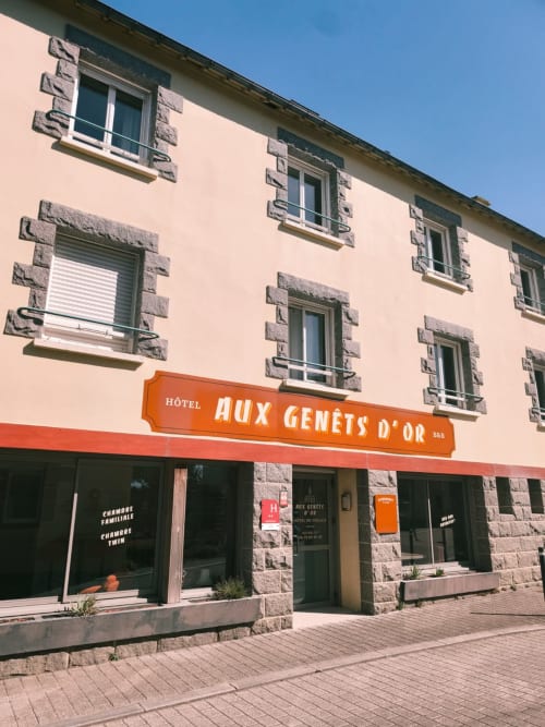Façade de l'hôtel Aux Genêts d'Or à Trévé avec murs pêche, détails en pierre et enseigne orangée
