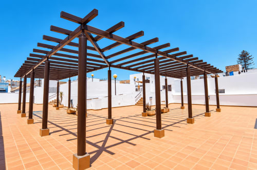Pérgola de madera moderna con vigas enrejadas en terraza de baldosas de barro del hotel Living Sur en Sanlúcar de Barrameda, España