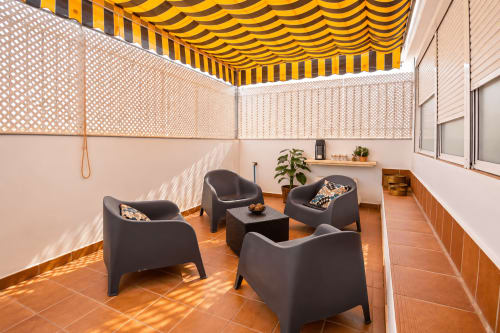Terraza de la Suite Castelar en Living Sur con tumbonas negras, toldo amarillo rayadoy suelo de terracota en Sanlúcar de
