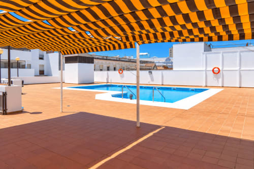 Área de piscina en la azotea del hotel Living Sur en Sanlúcar de Barrameda con piscina azul, sombrilla de rayas amarillas y blancas