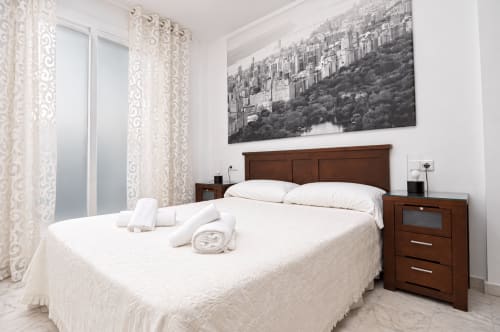 Habitación moderna en la Suite Castelar del hotel Living Sur en Sanlúcar de Barrameda con cama de madera, ropa de cama blanca y vistas al skyline de la ciudad