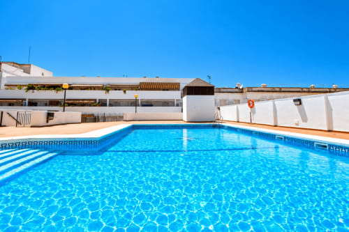 Piscina resplandeciente azul en el hotel apartamentos Living Sur de Sanlúcar de Barrameda con edificios blancos y cielo despejado