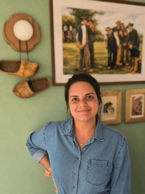 Femme en chemise en jean souriante à l'hôtel Aux Genêts d'Or à Trévé, France, avec décor rustique et portrait familial en arrière-plan