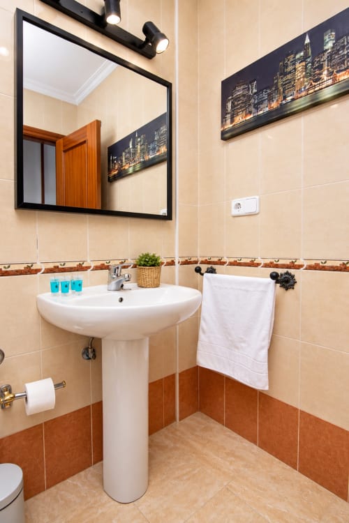 Baño moderno en la Suite Castelar del Living Sur Sanlúcar de Barrameda con lavabo de pedestal, espejo y detalles en azulejos marrones