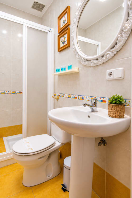 Baño infantil luminoso en la Suite Castelar con piso amarillo, lavamanos pedestal blanco, inodoro y ducha walk-in