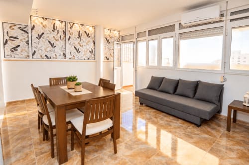 Luminosa sala de estar moderna en la Suite Castelar de Living Sur, Sanlúcar de Barrameda, con mesa de comedor de madera, sofá gris y