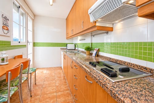 Cocina de la Suite Castelar en Living Sur con muebles naranjas, encimeras de granito, azulejos verdes y zona de comedor