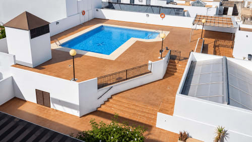 Piscina y terraza en la azotea de Living Sur en Sanlúcar de Barrameda con piscina azul, tarima de madera y apartamento blanco