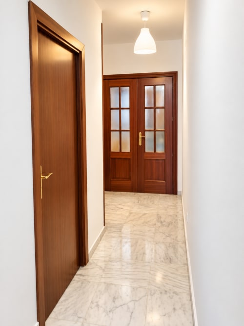 Pasillo luminoso en Suite Castelar de Living Sur, Sanlúcar de Barrameda, con piso de mármol, puertas de madera y lámpara colgante