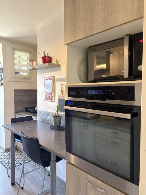 Cuisine moderne avec électroménagers en acier inoxydable, micro-ondes, four et table de salle à manger avec chaises noires au Cocon Arlésien à Arles