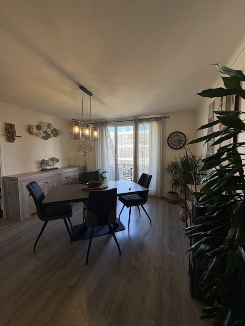 Salle à manger moderne du Cocon Arlésien à Arles avec chaises noires, table en bois, luminaires suspendus et vue sur la ville depuis le balcon