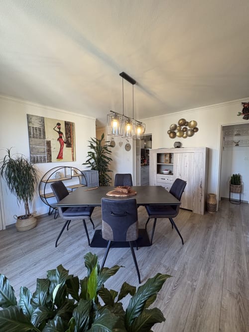 Salle à manger contemporaine de l'appartement Le Cocon Arlésien à Arles, avec table noire, chaises bleu marine, luminaires suspendus et espaces de vie