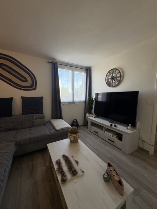 Salon moderne à la Conciergerie Maurin à Arles avec canapé gris, télévision, horloge et vue sur la ville